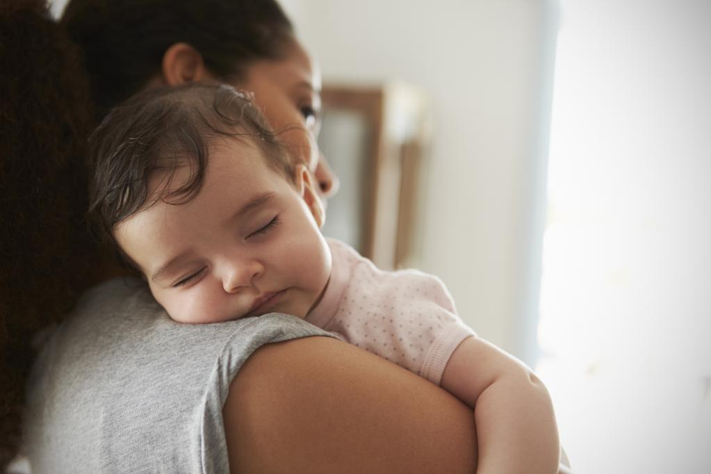 Photo of a mum holding a young sleeping baby on her shoulder.