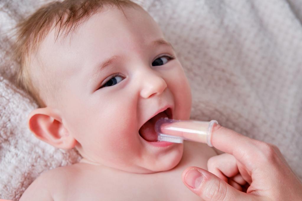 Photo of a small baby with their parent finger in their mouth cleaning their teeth