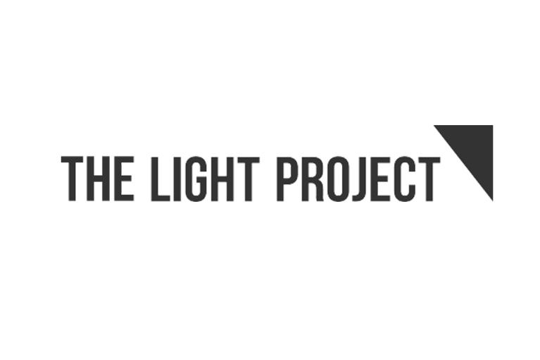 The Light Project logo features minimalist black text spelling out "THE LIGHT PROJECT", with a small black triangle accent in the top right corner.