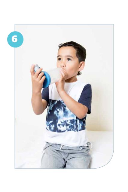 Photo of a child holding a spacer with an inhaler attached to the end and taking a deep breath