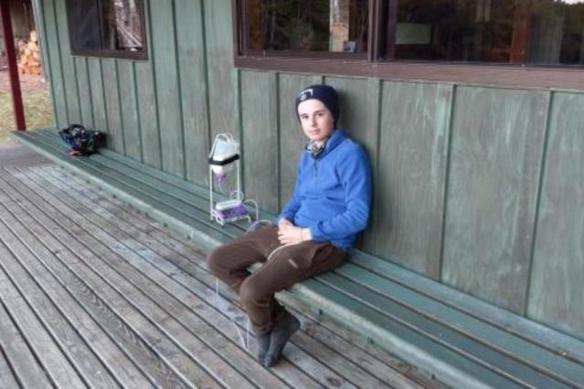 Photo of Alex on a day walk sitting at a hut next to his tube feeding equipment 