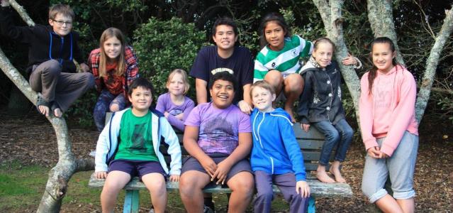 Group of 10 children sitting on and around a park bench