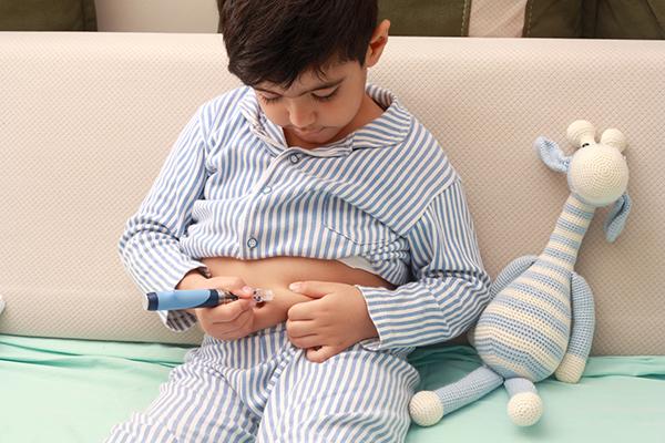 A photo of a young boy in blue striped pajamas injecting himself with insulin into his belly