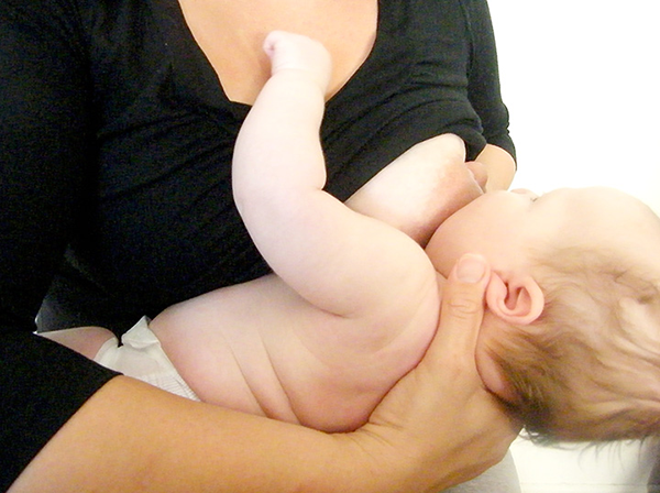 Mother breastfeeding her baby, positioned in cross-cradle hold. 