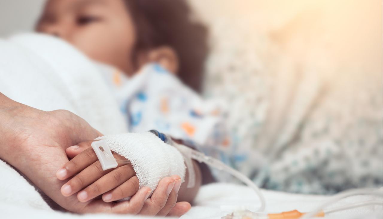 Photo of a child with a cannula in their hand in a hospital bed