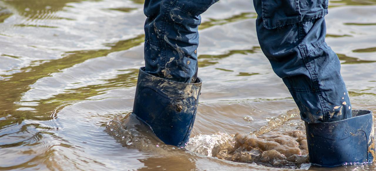 A person's legs with gumboots shown walking through flooding