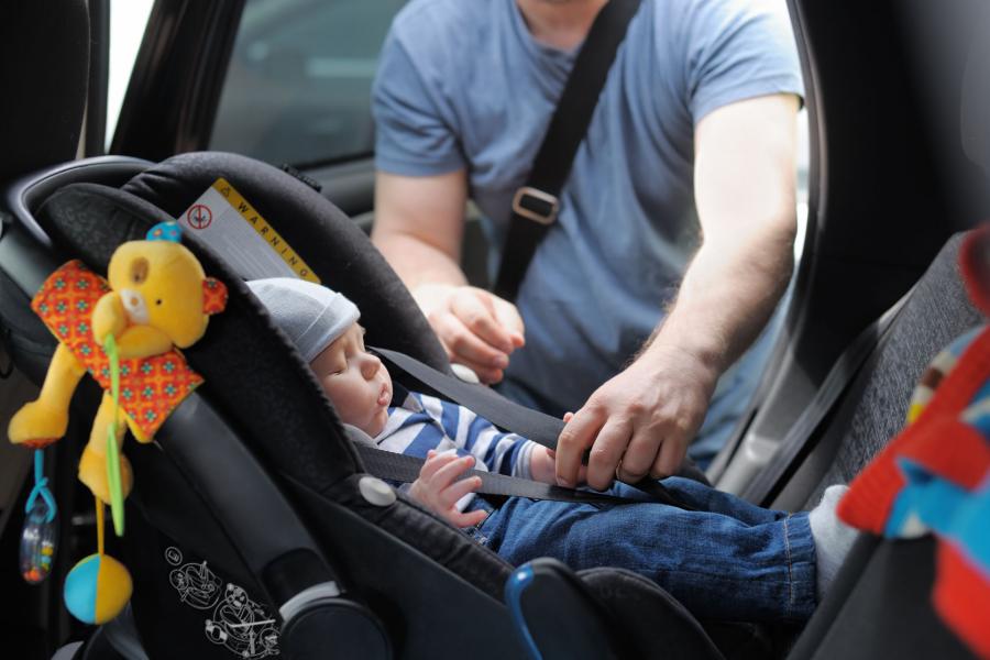 Father fastening his baby son in to a car seat