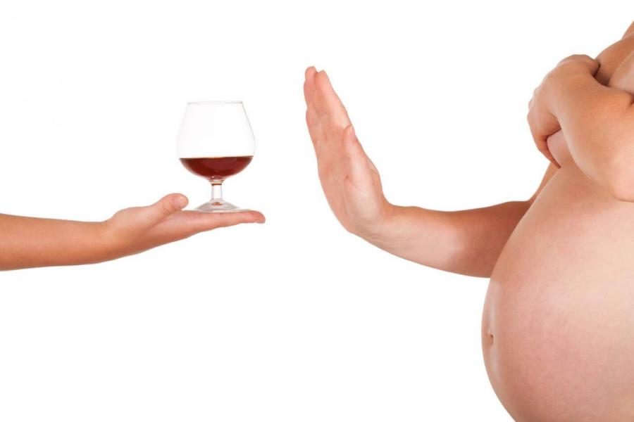 A mother's pregnant tummy signalling no with her hand to a glass of wine held out for her