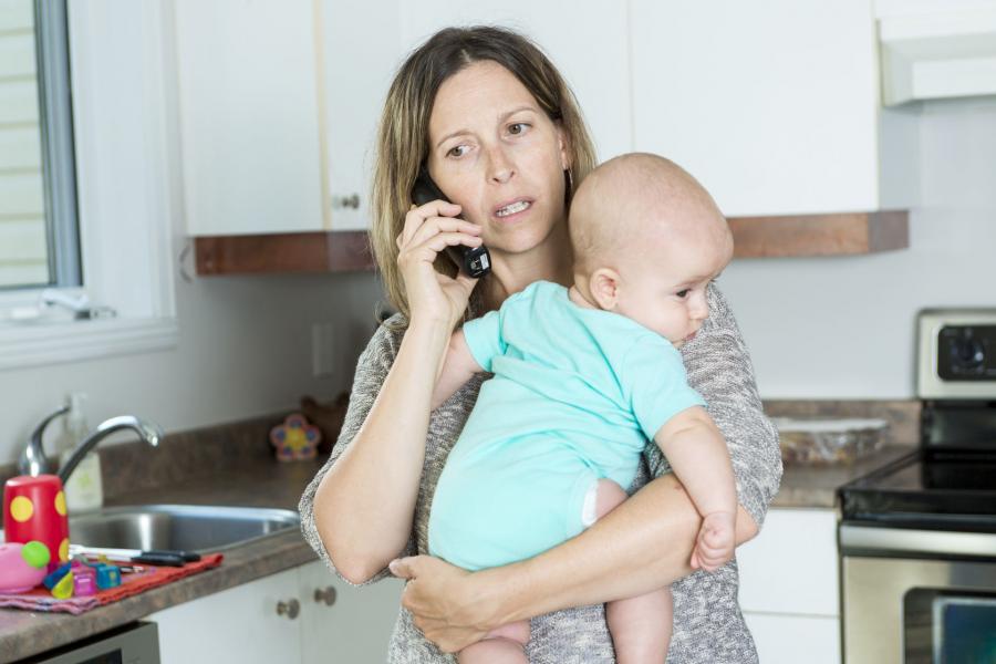 Mother on phone in kitchen holding her baby in her arms