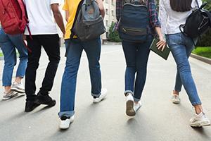 The back view of legs of five teens as they walk with bags and backpacks