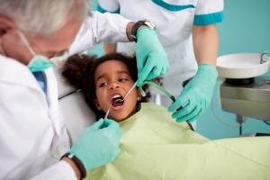 dentist examines child's teeth, child sitting in dentist's chair 