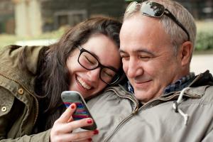 Father and teenage daughter looking and laughing at something on a mobile phone